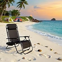Black reclining beach chair on sandy beach with palm trees and ocean view during sunset or sunrise.